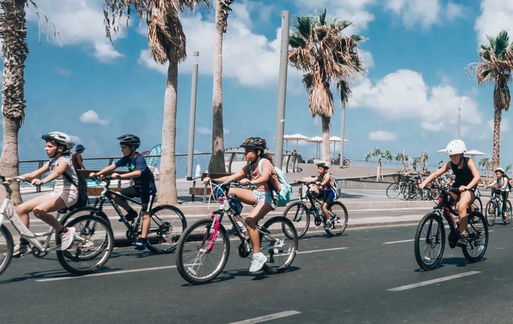 niños y niñas montando en bici por la ciudad cerca del mar con palmeras