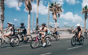niños y niñas montando en bici por la ciudad cerca del mar con palmeras